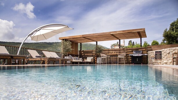 Zona junto a la piscina con sillones de descanso, una parrilla y una pérgola que proporciona sombra.