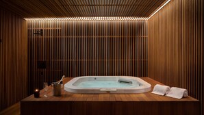 Un cuarto de spa con pared de listones de madera, un jacuzzi, una vela y una toalla sobre un banco de madera.
