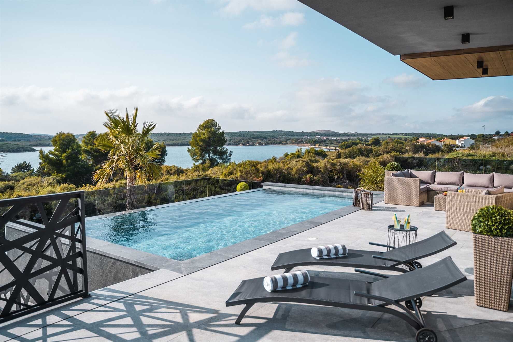 A rooftop infinity pool with lounge chairs and a view of a lake and hills.