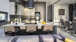 A modern kitchen with a central island, built-in appliances, and a dining area with leather chairs. - Villa La Vie with Pool (Medulin)
