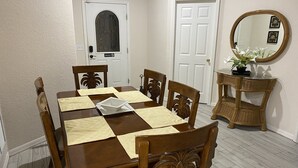 Una sala da pranzo con un tavolo di legno apparecchiato per quattro persone, una porta bianca con una finestra e uno specchio a parete.