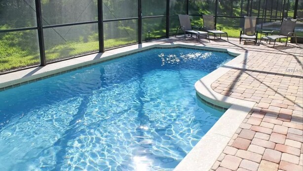 Una piscina con acqua cristallina, circondata da un patio in mattoni e riparata da una grande struttura in vetro.
