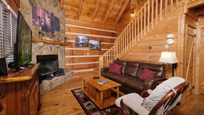 Interior acogedor de una cabaña con chimenea de piedra, paredes de madera, sofá de cuero y televisor.