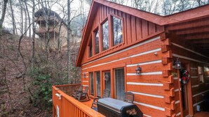 Una cabaña de troncos con una terraza, una parrilla y vistas a un bosque.