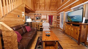 Un interior acogedor de cabaña con detalles de madera, un sofá de cuero marrón, una mesa de centro de madera y un televisor sobre un mueble de madera.