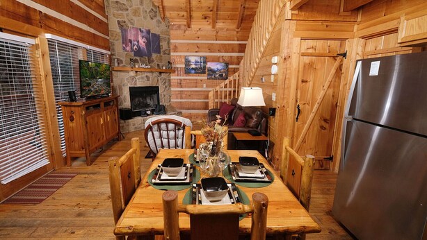 Interior acogedor de una cabaña con chimenea de piedra, una mesa de comedor de madera y un refrigerador moderno de acero inoxidable.