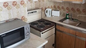 A compact kitchen with a microwave, stove, kettle, and sink. - Apsley House Flat 1 - 4 Berth (Great Yarmouth)