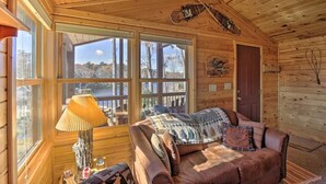 A cozy cabin interior with a wooden ceiling, a large window, a leather couch, and a lamp. - Secluded Waterfront Cabin on hiking trails! Lake on one side river on the other. (Luck)