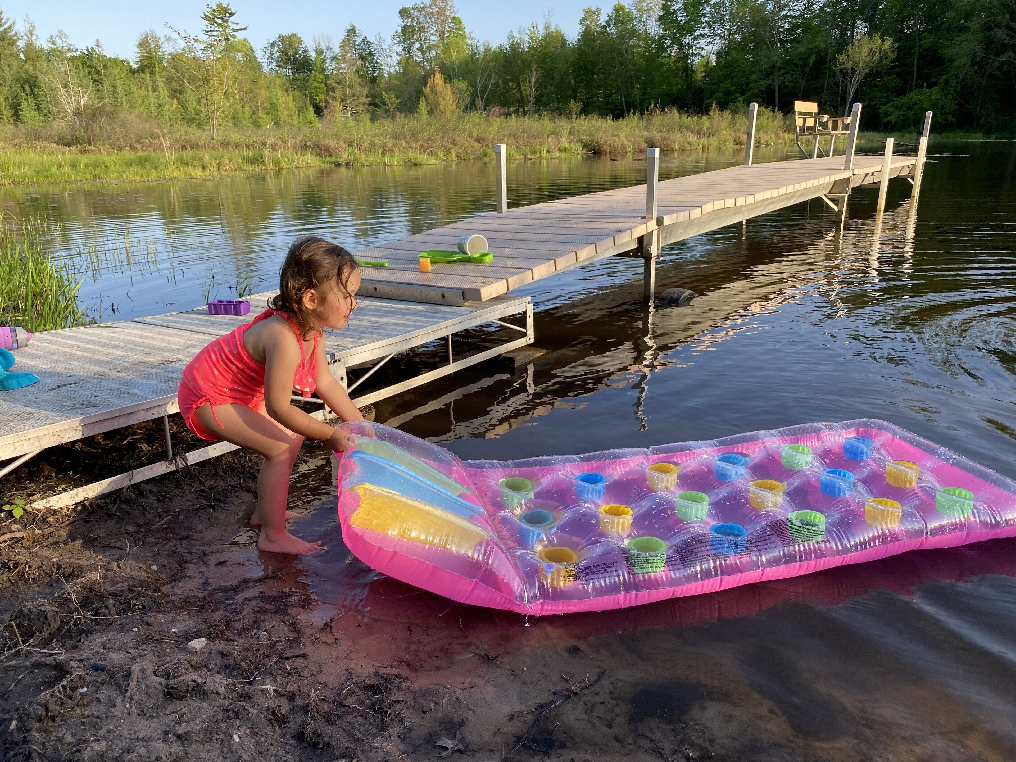 A wooden dock extending into a calm body of water, with a child playing near the edge.