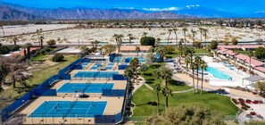 An aerial view of a resort with multiple tennis courts, a swimming pool, and a mountainous backdrop.