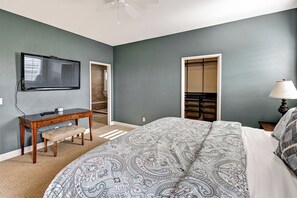 A bedroom with a bed, a desk, a chair, a television, a wardrobe, and a lamp.