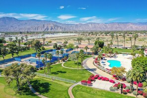 Un resort con varias canchas de tenis, una piscina y un telón de fondo montañoso.