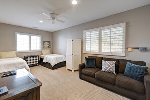 A bedroom with two beds, a sofa, a desk, and a ceiling fan.