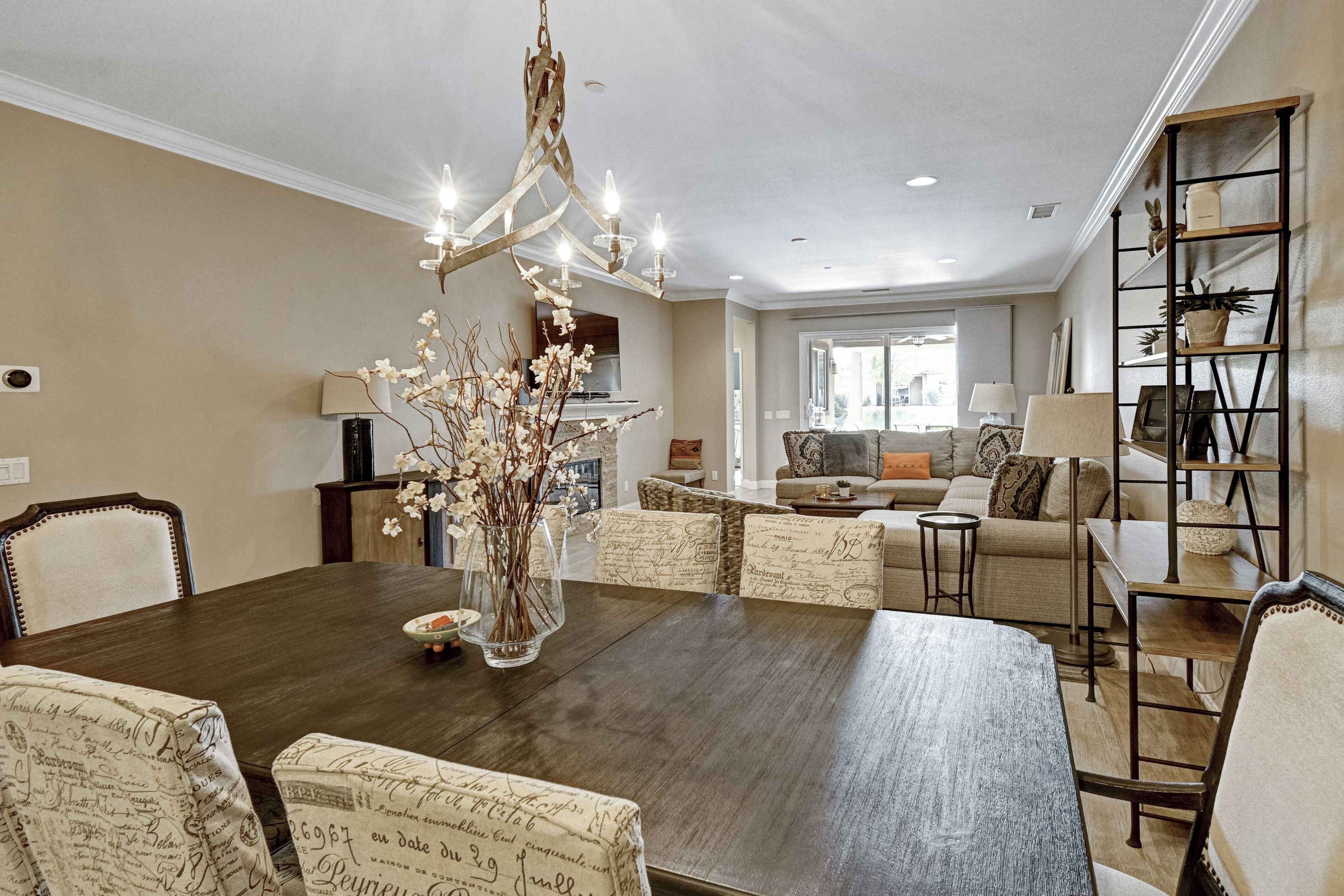 A dining area with a dark wooden table, white upholstered chairs, and a chandelier.