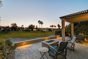 An outdoor patio area with a pergola, seating, and a well-maintained lawn.
