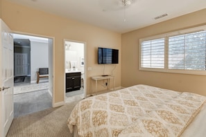 A bedroom with a bed, a television on the wall, and a window with blinds.