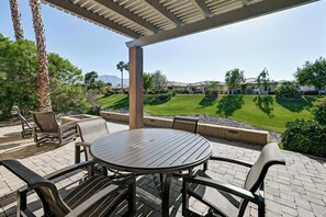 Un patio exterior con una mesa redonda y sillas, rodeado de un jardín ajardinado y vistas a una zona residencial.