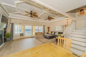 Relax in this spacious living area with a high ceiling, featuring a dining table, sofa, and armchair, with a staircase leading to an upper level and a fireplace.