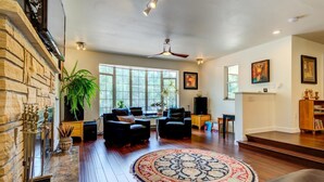 A spacious living room with a large window, a fireplace, and a ceiling fan. - INNhale Bed&Brunch in Manitou Springs (Manitou Springs)