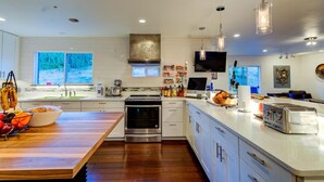 A modern kitchen with a wooden island, stainless steel appliances, and a large window overlooking a forested area. - INNhale Bed&Brunch in Manitou Springs (Manitou Springs)