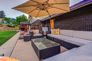 An outdoor patio with wicker furniture, a glass-top table, and a large umbrella.