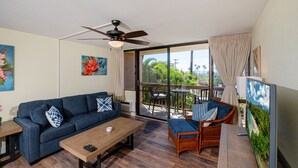 A living room with a sofa, a coffee table, a ceiling fan, and a view of the outdoors.