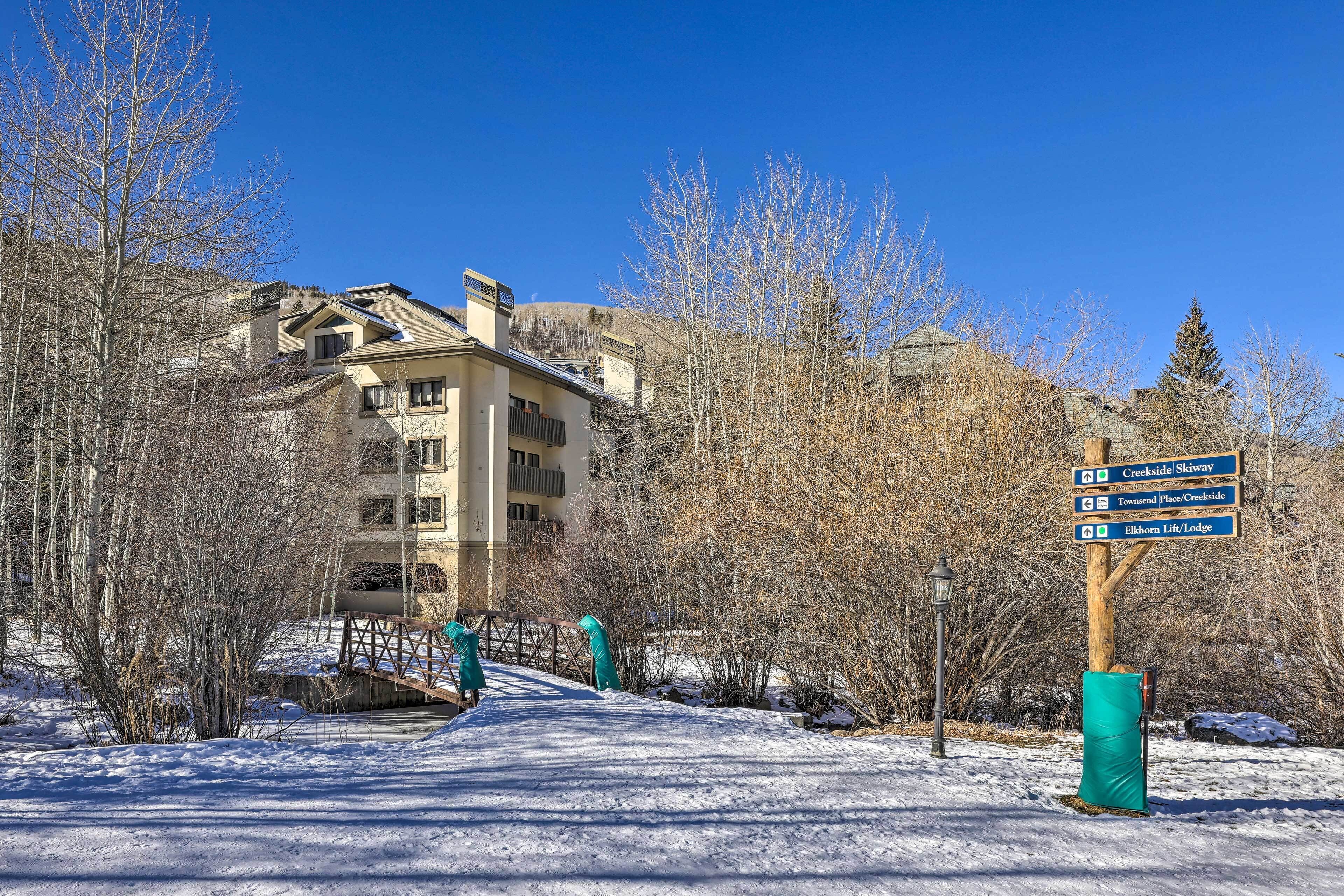 A snow-covered path leading to a building with a signpost indicating directions to Creekside Skiyway, Townend Place/Creekside, and Elkhorn Lift/Lodge.