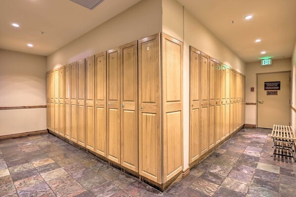 A row of wooden lockers in a hallway with a tiled floor and an exit sign.