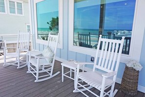 Une terrasse en bois avec des fauteuils à bascule blancs et un panier en osier.