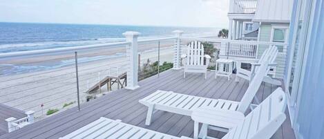 A wooden deck with white lounge chairs overlooking a beach.