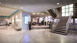 A spacious lobby with a modern staircase, seating areas, and a digital display. - Thistle City Barbican (London)