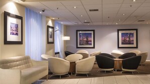A hotel lobby with a beige sofa, black and beige chairs, a small table, and framed pictures on the walls. - Thistle City Barbican (London)