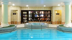 A large indoor swimming pool with a central hot tub, surrounded by beige tiled walls and columns. - Thistle City Barbican (London)