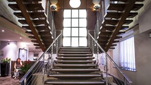 A modern staircase with glass railings, wooden beams, and a large window at the top. - Thistle City Barbican (London)