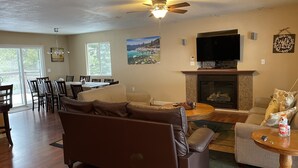 A living room with a brown sofa, a round coffee table, a fireplace, and a television mounted above it.