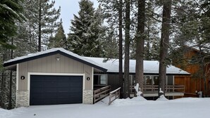 A two-story building with a garage, surrounded by tall trees and covered in snow.