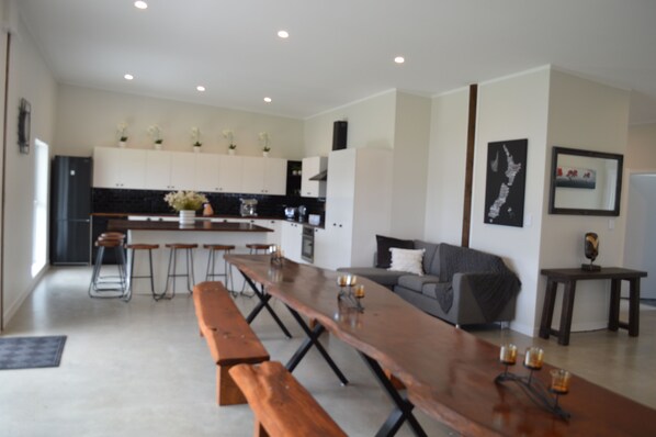 A modern kitchen with white cabinets, a long wooden table, and bar stools.