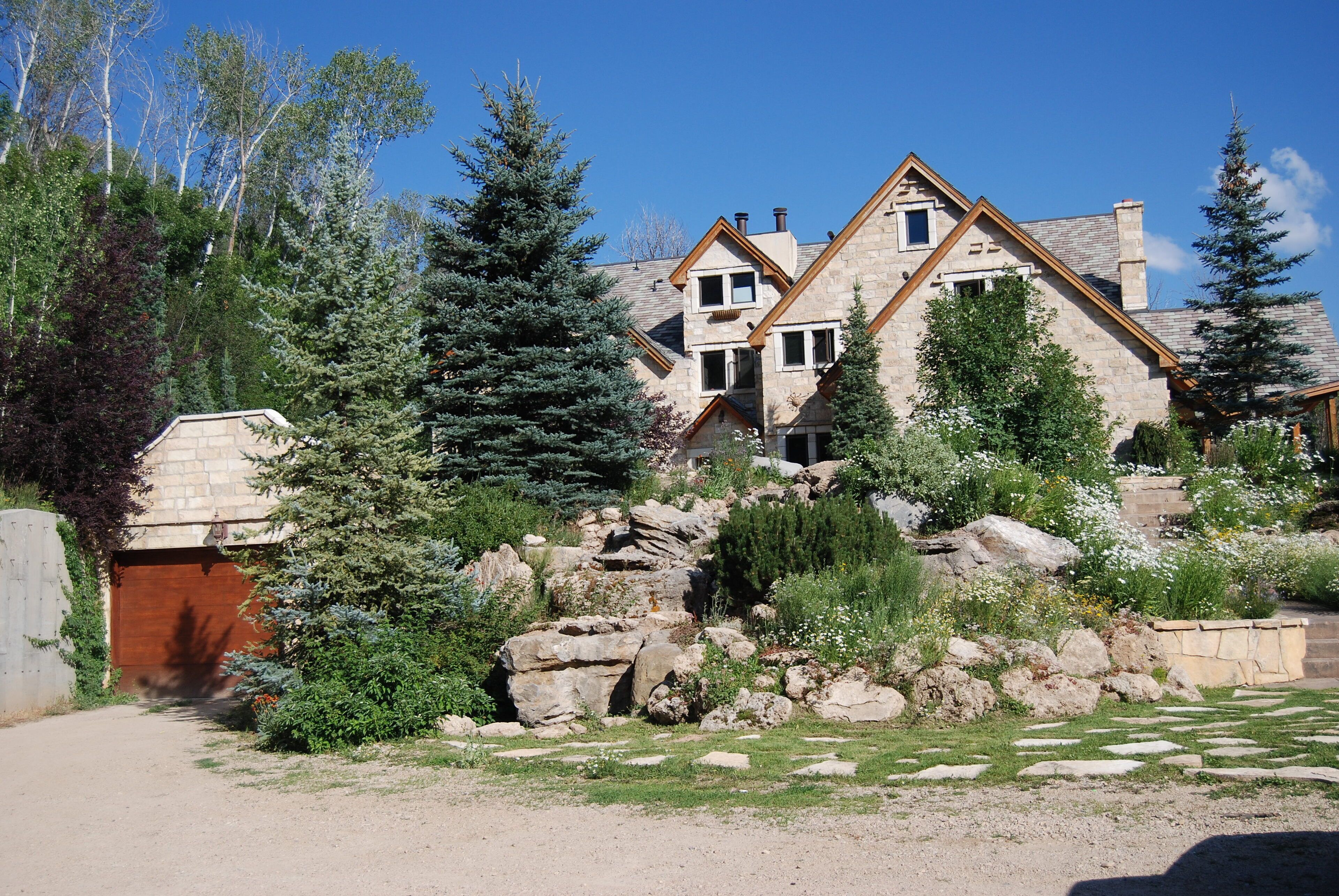 A stone house with a sloped roof, surrounded by a garden with rocks and trees.