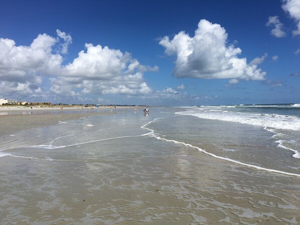 Une plage avec des vagues, un ciel dégagé et quelques personnes au loin.