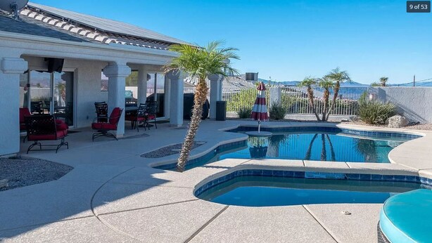 Une piscine à bord incurvé, entourée d’un patio aménagé avec des meubles d’extérieur et un palmier.