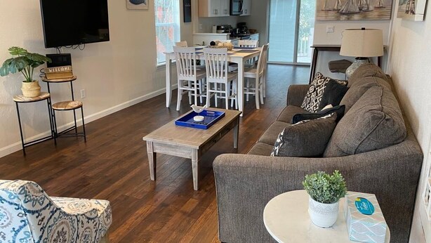A modern living room with a grey sofa, a round coffee table, and a dining area with white chairs.