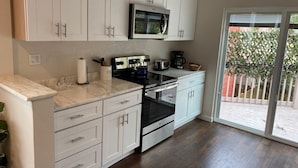 A modern kitchen with white cabinets, a built-in microwave, a stove, and a coffee maker.