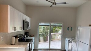 A modern kitchen with white cabinets, a microwave, a refrigerator, and a sliding glass door leading to a deck.