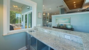 A kitchen with a large window, a wooden ceiling, and a countertop with a sink.