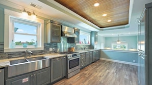 A modern kitchen with stainless steel appliances, a wooden ceiling, and large windows.