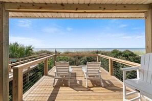 A wooden deck with two white Adirondack chairs facing a beach.
