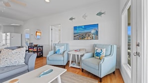 A modern living room with a gray sofa, two light blue armchairs, a coffee table, and a TV wall art depicting a coastal scene. - "After Dune Delight" oceanfront, 7 bedroom 3 bathrooms (Holden Beach)