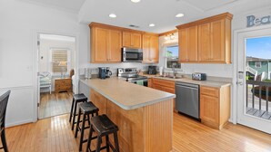 A modern kitchen with wooden cabinets, stainless steel appliances, and a central island with bar stools. - "After Dune Delight" oceanfront, 7 bedroom 3 bathrooms (Holden Beach)