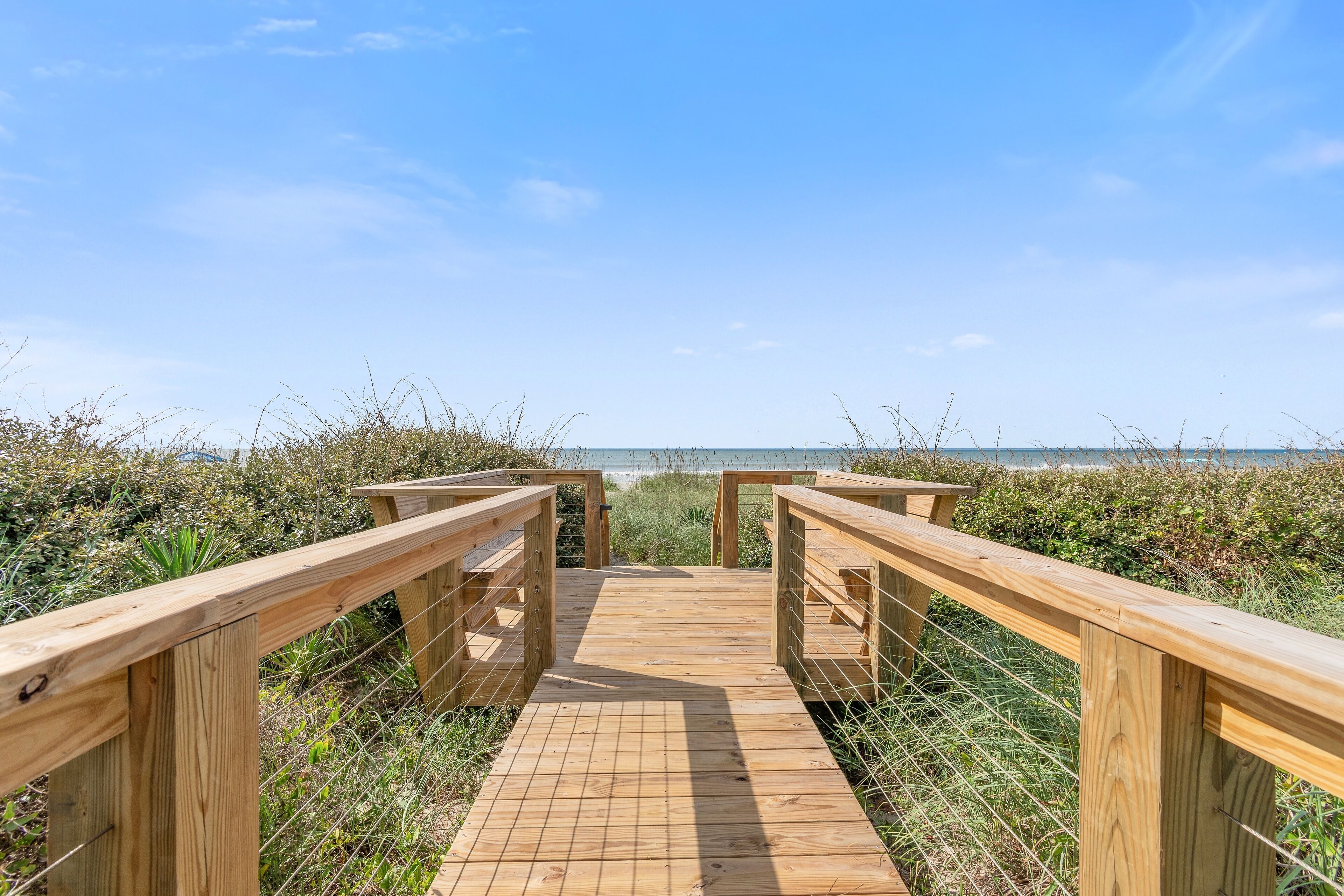 A wooden boardwalk leading to a beach with a clear sky.