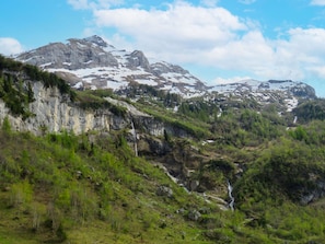 A mountainous landscape with a waterfall, rocky cliffs, and sparse vegetation.